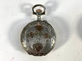 two silver pocket watches sitting on a white surface