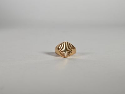une bague en forme de coquillage dorée sur un fond blanc