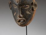 un masque en bois au visage noir, posé sur un socle