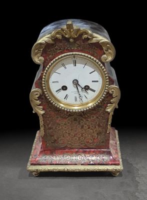 une horloge rouge et dorée posée sur un socle, sur fond noir