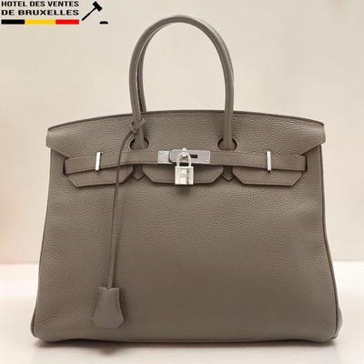un sac à main en cuir gris posé sur une table blanche