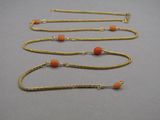 four gold chain necklaces with coral beads on a gray surface
