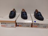trois paires de chaussures noires posées sur des cartons, sur une surface blanche