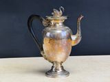 an antique silver tea pot with a black handle on a wooden table