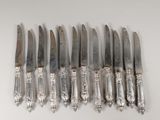 six silverplated knives are lined up in a row on a white surface
