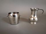 un pichet en métal argenté et une coupe en argent posés sur une table