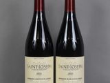 two bottles of wine sit on a glass table in front of a gray wall