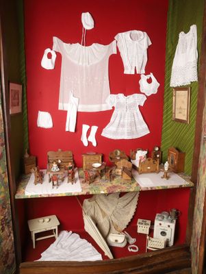 une maison de poupées avec des vêtements posés sur une étagère dans un coin