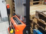 un chariot élévateur orange et noir dans un entrepôt rempli de palettes, les unes à côté des autres