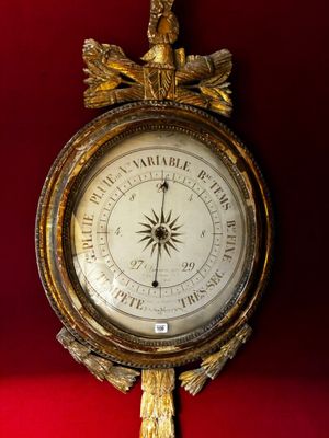 une horloge dorée accrochée à un mur rouge, sur laquelle est représenté un oiseau