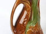 a brown and green vase with a handle on a white surface