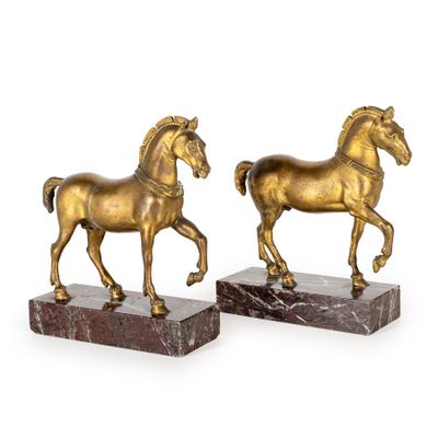une paire de statues de chevaux en or sur des socles en marbre, sur fond blanc