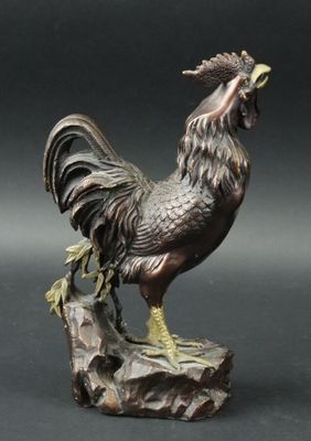 bronze statue of a rooster on a rock with a black background