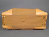 tan leather handbag with gold studded handles on grey background