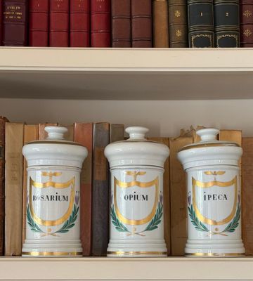 three white jars on a shelf with books in the background