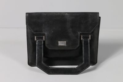 un sac en cuir noir muni d'une poignée métallique, posé sur une surface blanche