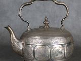 une vieille théière en argent avec une anse, posée sur une table