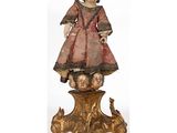 une statue ancienne en bois représentant une fillette avec une poupée, posée sur une table