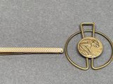 a gold tie bar with a coin on it