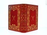 un livre rouge orné de motifs dorés, posé sur une surface blanche