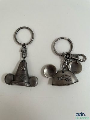 two metal mickey mouse keychais are shown on a white surface
