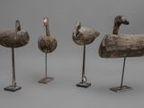 trois canards en bois sculptés posés sur des socles, sur fond gris