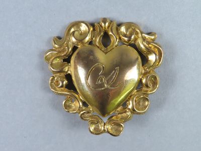 an image of a gold heart shaped brooch with a monogram on it