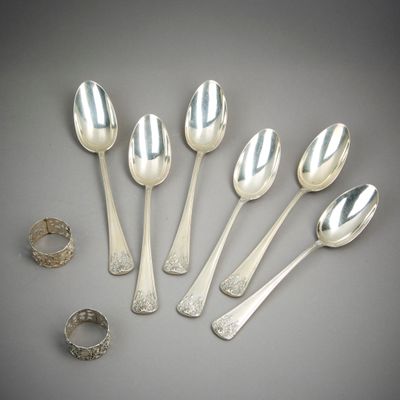 six cuillères en argent et une bague posées sur une surface grise
