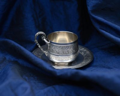 a silver cup and saucer sitting on a blue cloth