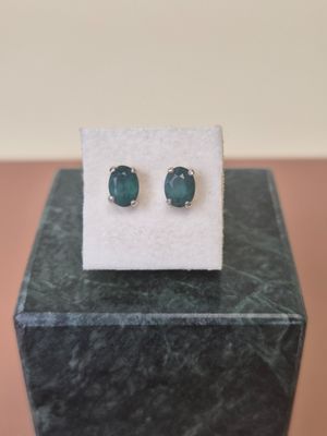 a pair of emerald stone stud earrings sitting on top of a marble block