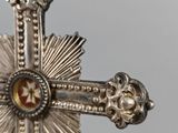 silver cross with a red and yellow stone in the center