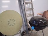 a large black grill sitting in a garage next to a ladder