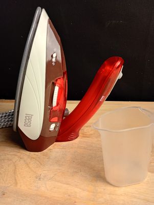 un fer à repasser rouge et blanc posé sur une table, à côté d'un verre d'eau