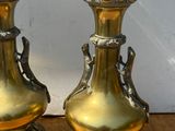 deux vases en or posés sur une table, avec un mur blanc en arrière-plan