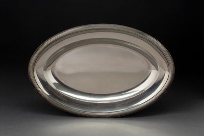 une assiette ovale en argent posée sur une surface noire