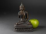 statue of a person sitting in a lotus position with a green apple in the foreground