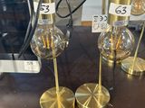 two gold lamps on a table with price tags on them
