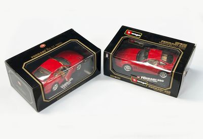 une paire de petites voitures rouges moulées sous pression, dans des boîtes noires sur fond blanc