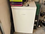 a small refrigerator in the corner of a room with a lot of clutter on the floor