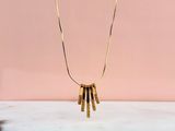un collier en or auquel sont suspendus cinq lingots d'or, sur fond rose