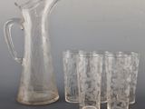 four glasses and a pitcher sitting next to each other on a table