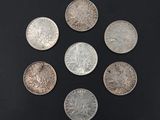 six different types of silver coins on a black surface