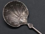 an antique silver spoon with a shell shaped handle on a black surface