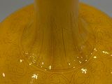 a yellow vase sitting on a table with a gray background