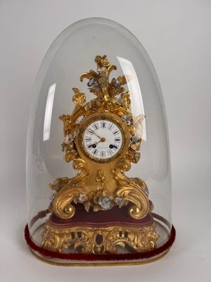 a gold clock under a glass dome on a white surface