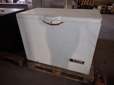 un congélateur coffre blanc posé sur une palette dans un entrepôt