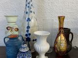 de nombreux vases de styles variés posés sur une table, avec un mur blanc en arrière-plan