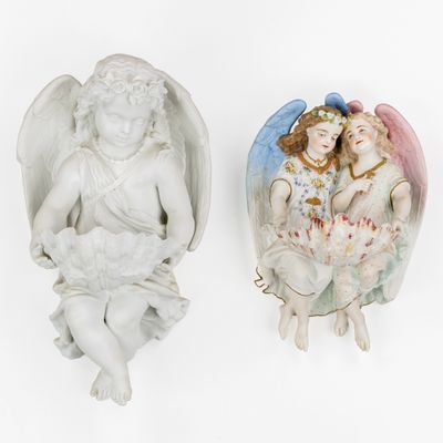 two figurines of angels sitting on a white surface