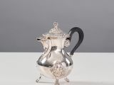 une cafetière en argent avec une poignée noire posée sur une table
