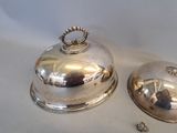 two silver plate covered dishes sitting on top of a white table
